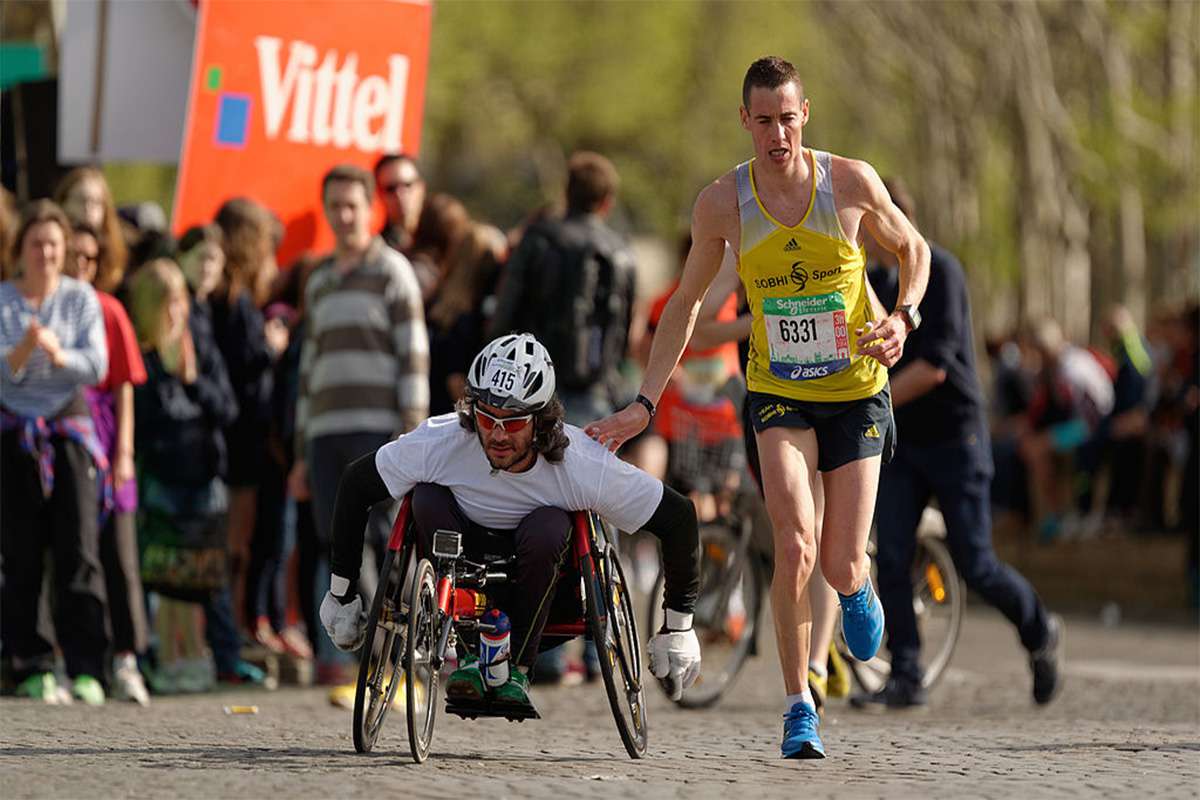 A runner gives a friendly tap on the shoulder to a wheelchair racer during the Marathon International de Paris (Paris Marathon) in 2018